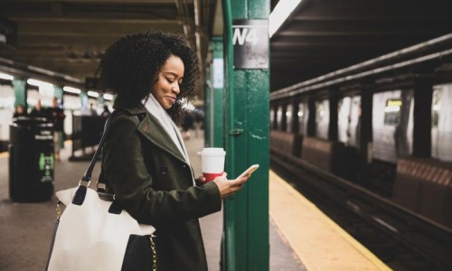woman with a cup of coffee texts on subway station platform